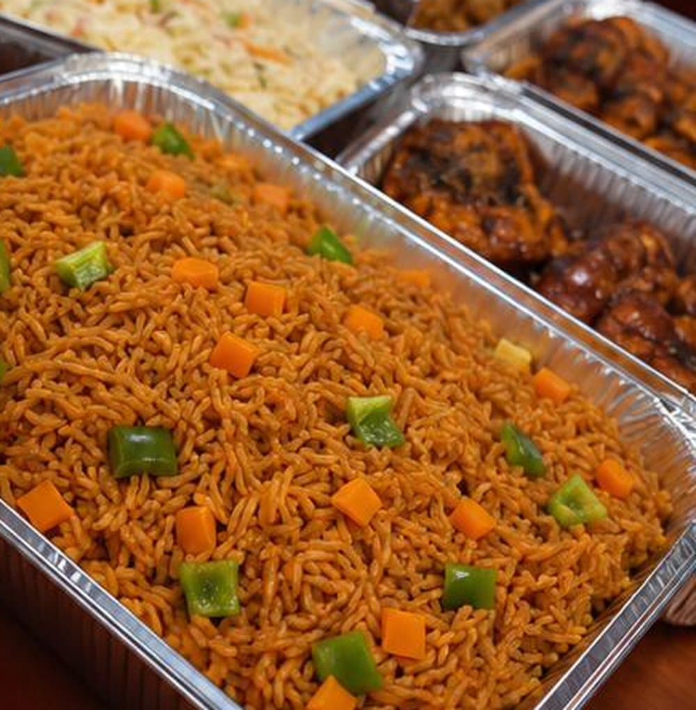 Trays of Ghanaian jollof rice with diced carrots and green peppers, vegetable rice and grilled chicken, prepared by Phali's Flavor House in Madina, Accra